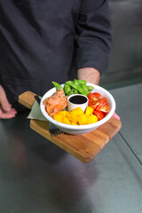 Unrecognizable chef showing fresh colorful poke bowl with salmon on restaurant kitchen