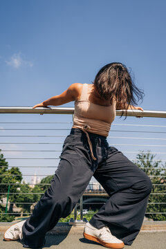 Dancer leans powerfully against a bridge railing under a bright sky