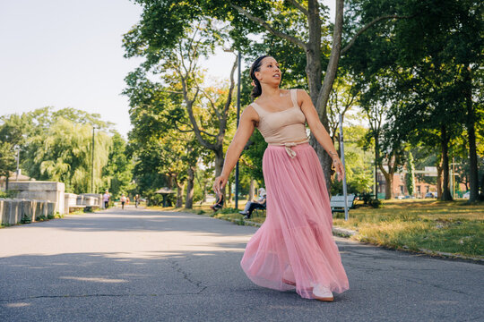 Woman dancing gracefully in park wearing long pink skirt