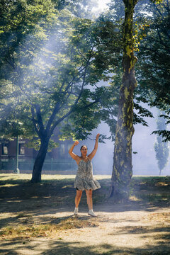 Woman dancing spontaneously in sunlit park with smoke