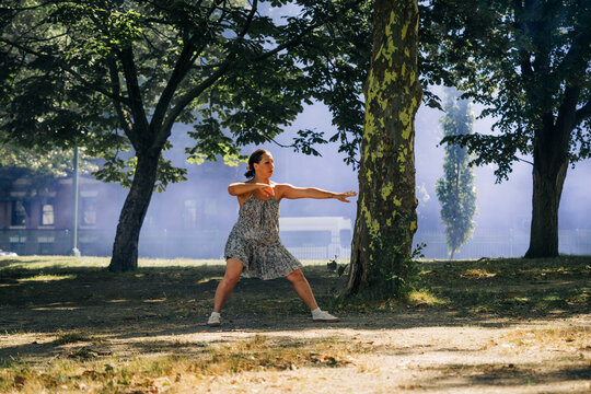 Woman holds powerful dance pose in shaded urban park setting