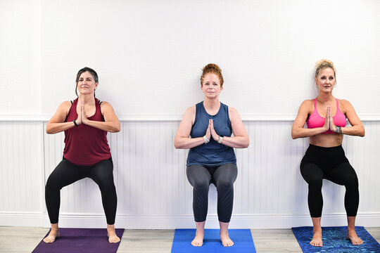 Three women doing wall sits in yoga class with hands in prayer p