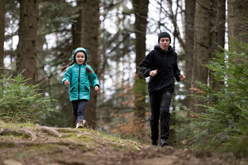 Obraz premium Two children enjoy a brisk run through a lush woodland trail on a cool, overcast day, cultivating a spirit of adventure in the heart of nature