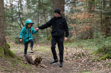 Together in nature walking through a wooded trail as a child balances on a log with her older...
