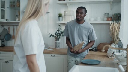 Cute lovers communicating in kitchen in morning when cleaning and washing dish. Interracial married couple communicating or quarrelling, happy spouses doing housework together, gender equality - Powered by Adobe
