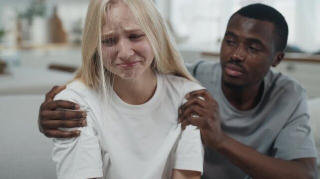 Blonde woman crying when quarreling with husband, black man hugging his wife. Interracial marriage, loving couple swearing in apartment, diversity and unity of people, different races and culture