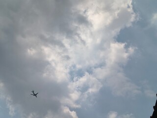 Commercial airplane flying through cloudy sky with architectural silhouette in foreground