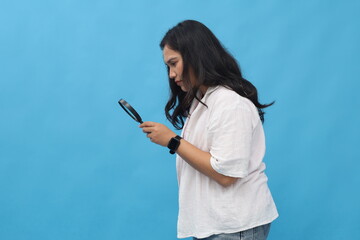 Young Asian female detective looking through magnifying glass with curious gaze, serious...