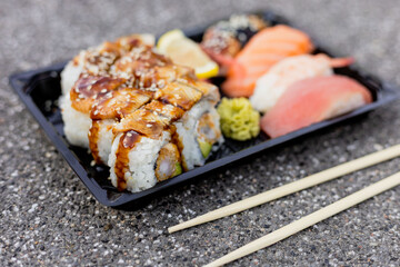 A carefully arranged sushi platter showcases various rolls topped with sauce and pieces of sashimi. The vibrant colors and textures are appealing, served with chopsticks