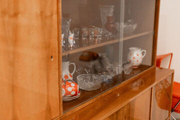 A wooden cabinet showcases various pieces of vintage glassware and ceramics, including pitchers and...