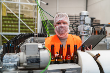 Worker observing bottles on a conveyor belt in a beverage factory, ensuring quality during the beer production process