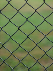 Fototapeta premium Close-Up of Chain Link Fence with Shallow Depth of Field - Metal Wire Mesh Barrier with Blurred Green Background
