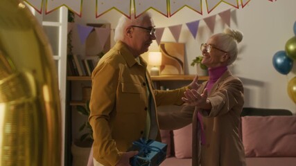 Happy elderly woman meeting old friends coming to her birthday party, she hugging them and inviting to living room