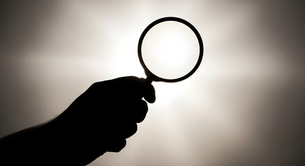 A silhouette of a hand holding a magnifying glass against a bright light source symbolizing search and discovery