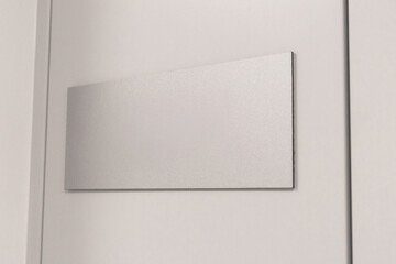 A blank, rectangular signboard rests on a smooth white wall, commonly found in contemporary spaces. This sign could be used for labeling or decorative purposes in various environments