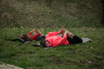 Practicing yoga outdoors with children enjoying relaxation and flexibility exercises on a grassy patch under a serene sky in early morning light