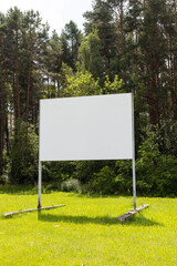 A large blank billboard is placed in the middle of a vibrant green field, bordered by tall trees. The scene is serene and peaceful, suggesting potential for advertisement or information