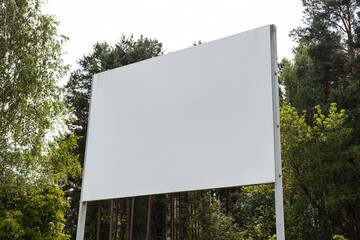 A large blank billboard is positioned in a green forest area surrounded by trees. The bright daylight illuminates the space, creating a peaceful atmosphere