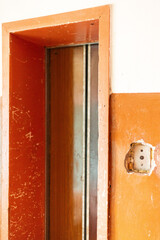 Inside an old house, the walls are peeling and damaged. An elevator shaft with rusty doors is visible, signifying years of neglect in this seemingly abandoned space