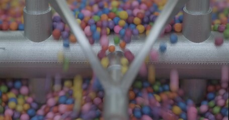 Industrial mixer mockup mixes multi-colored pieces of plastic. Handheld close up shot, real time speed, artificial indoors lighting.