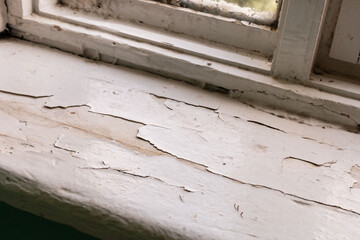 Window sill of an old house reveals significant damage with peeling paint and discoloration. The scene reflects years of neglect and the need for repairs in this aging space