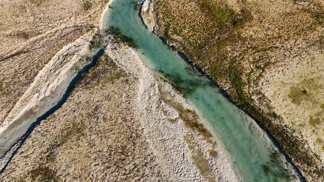 Aerial top down view of a turquoise river splitting into two branches creating a y shape pattern flowing through a dry barren gravel and dirt landscape during daylight without people