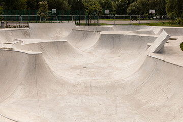 A spacious skate park features smooth concrete curves and ramps, inviting skaters to practice tricks and enjoy the vibrant green surroundings. It is a sunny day, ideal for outdoor fun