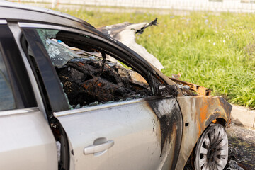 A car heavily damaged by fire is seen on the roadside. The metal is burnt and blackened, amidst...