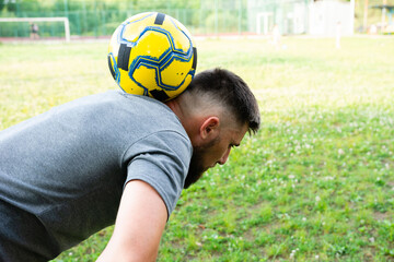 Man balancing soccer ball on his neck, outdoors. Focused expression, athletic build.