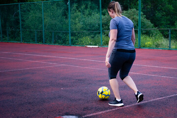 Woman playing soccer on a red court. She kicks a yellow ball, enjoying outdoor exercise.
