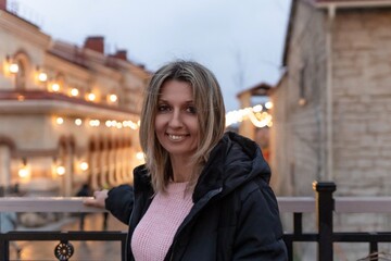 Woman smiling evening portrait in city square illuminated by warm string lights enjoying winter...