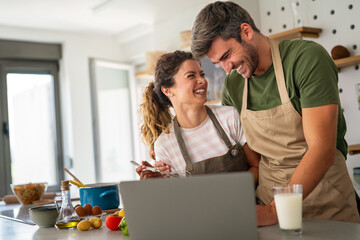 Young couple using laptop computer to take part in online culinary workshop, cooking together