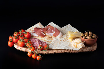 Antipasto con prosciutto, formaggio e olive su pane carasau su sfondo nero