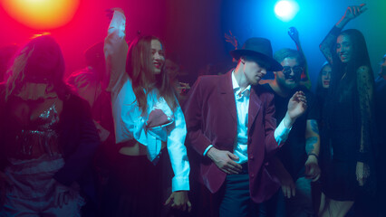 Halloween party crowd dancing in neon lights with costumes and masks. Concept of entertainment, holiday advertising, youth culture and emotional nightlife.