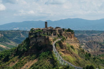 Fototapeta premium Civita di Bagnoregio, in central Italy, features medieval stone buildings, a prominent bell tower, and breathtaking views of surrounding valleys and mountains.