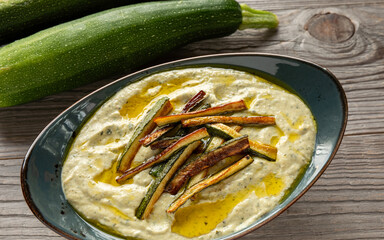 Dip made of braised courgette and tahini, decorated with fried zucchini strips. Whole, fresh courgettes at the back. Rustic wooden background. Middle Eastern cuisine.