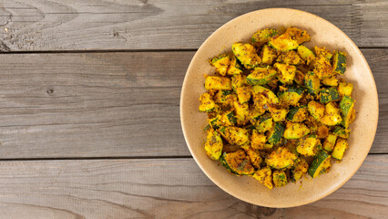 Fried zucchini breaded in chickpea flour. A vegan Indian side dish made of zucchini coated with chickpea flour and stir-fried. Rustic wooden background with copy space.