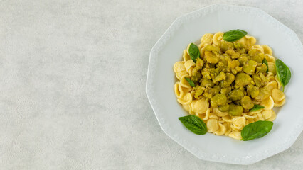 Orecchiette pasta with braised broad beans and basil. A classic Italian dish called pasta e fave or pasta con fave. White, textured background with copy space.