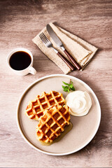 焼きたてワッフルとホイップクリーム、メープルシロップを添えたティータイムのひととき。木のテーブルに置かれた白いプレートに、コーヒーと麻のナプキン、カトラリーを添えた温かみのあるブランチシーン