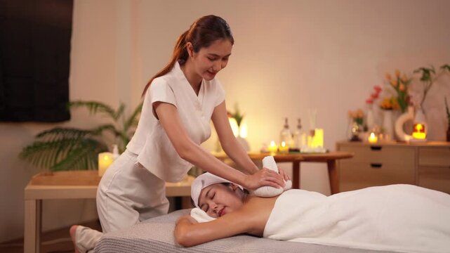 Asian adult women enjoy soothing herbal compress massage treatment at luxury wellness spa for deep relaxation and body care