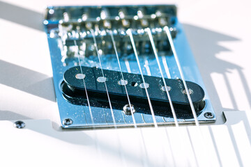 Closeup of an electric guitar bridge and single-coil pickup, with metallic saddles and strings casting sharp reflections. It highlights the technical precision of guitar construction