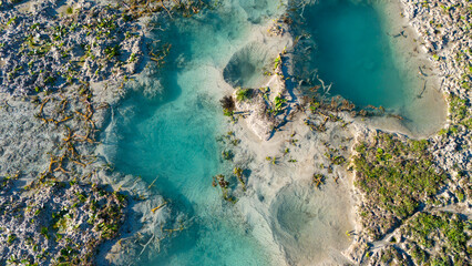 Aerial top view of a stunning natural water formation with clear blue hues surrounded by a rugged and textured landscape showcasing the raw and wild beauty of our planet