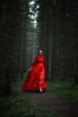 woman wearing a bright red dress gracefully strolls along a secluded path in a dense forest. tall trees create a serene and mysterious atmosphere