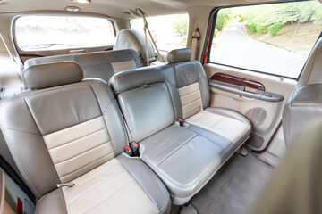 Rear two row beige leather bench seats, interior of an older 2004 American 4x4 family suv truck.   Shown in natural daylight, highlighting clean and well-preserved cabin details, speakers, armrests 