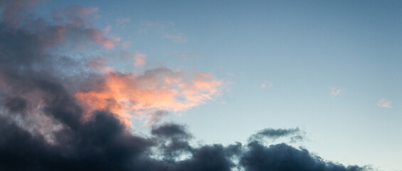 Obraz premium Horizontal shot of the sky with dark gray storm clouds against a soft blue-pink gradient before or after sunrise or sunset, creating a dramatic contrasting background