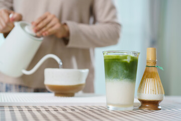 Close up of iced matcha latte on table with Asian woman making tea behind.