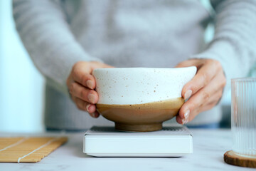Asian woman placing matcha bowl on digital weight scale.