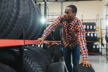 Male studying car tire in market. African american guy in casual wear stand looking at tire, make choice. shopping time