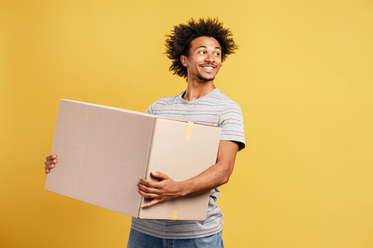 Smiling happy African American man holding caron box with mockup looking away