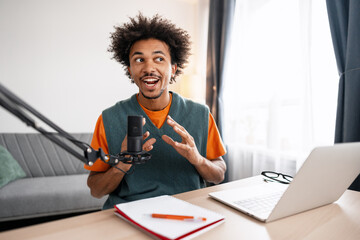 Handsome positive African American man talking using microphone and laptop, recording podcast